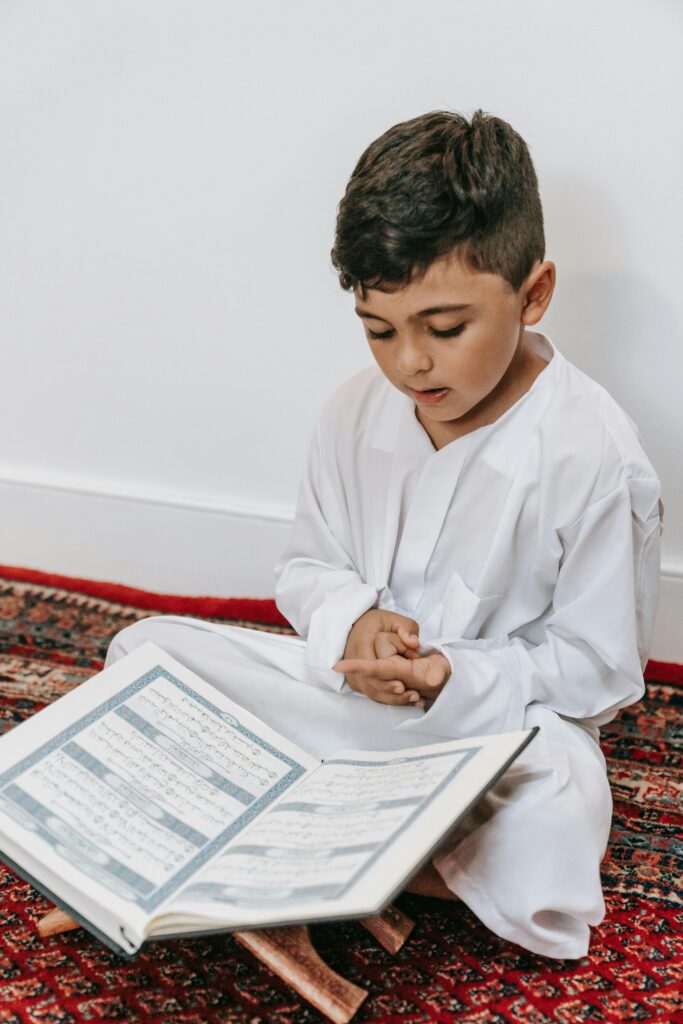 A young boy dressed in white reads the Quran, symbolizing cultural and religious devotion.